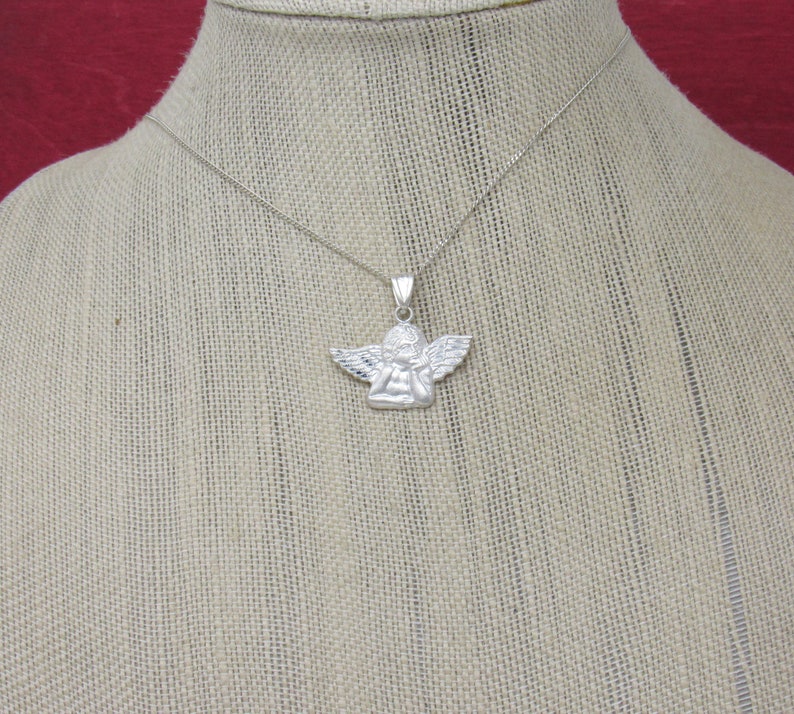 May include: A silver chain necklace with a small silver angel pendant. The angel is depicted with wings and a prayerful pose.