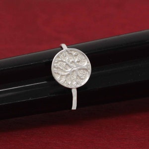 May include: A silver ring with a round tree of life design. The ring is on a black surface.