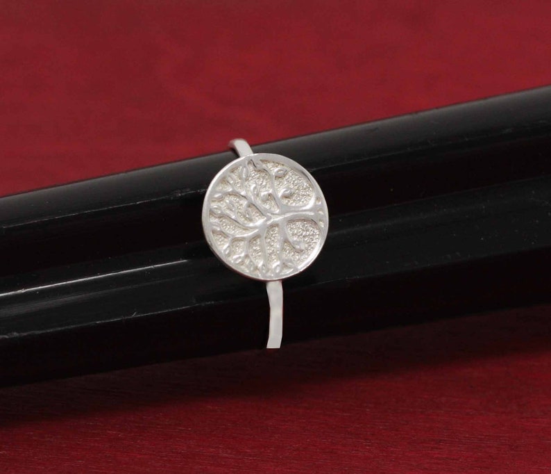 May include: A silver ring with a round tree of life design. The ring is on a black surface.