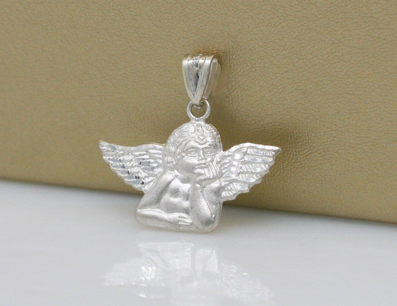 May include: Silver pendant featuring a cherub angel with wings, holding its chin in thought.