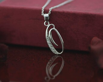 Può includere: Una collana con ciondolo in argento a forma di lettera O corsiva. La lettera è decorata con piccole pietre trasparenti.