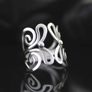 May include: A silver ring with a delicate, intricate design featuring swirling patterns. The ring is made of a smooth, polished metal and has a modern, minimalist aesthetic.