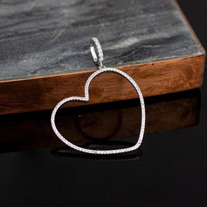 Op de afbeelding: Een zilveren hartvormige hanger met een heldere kristallen rand. De hanger hangt aan een zilveren ketting.
