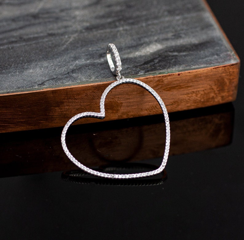 Op de afbeelding: Een zilveren hartvormige hanger met een heldere kristallen rand. De hanger hangt aan een zilveren ketting.