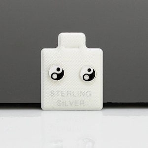 May include: A pair of sterling silver earrings featuring a black and white yin yang symbol design. The earrings are presented on a white card with the words "STERLING SILVER" printed on it.