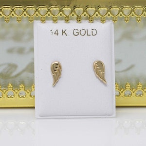 Puede incluir: Un par de pendientes de oro en forma de alas de &aacute;ngel en una tarjeta blanca con el texto "14K GOLD".