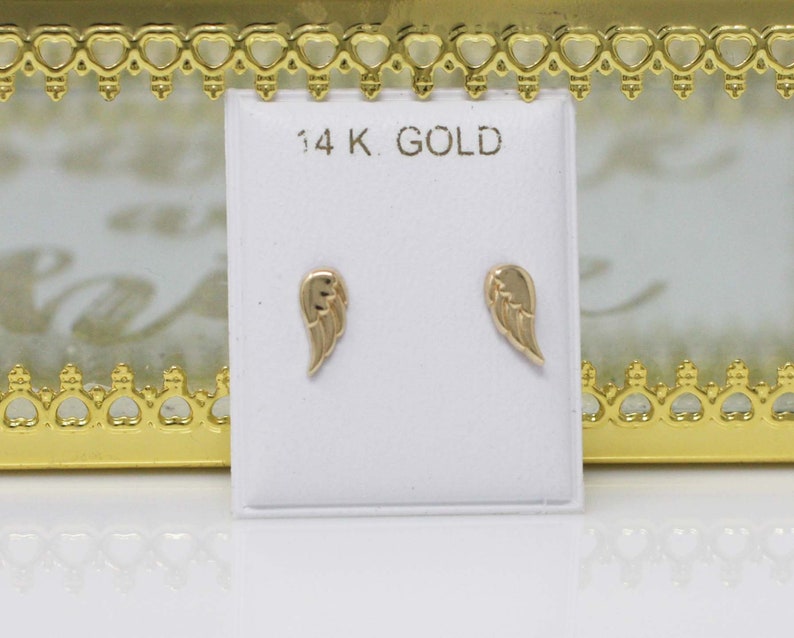 Puede incluir: Un par de pendientes de oro en forma de alas de &aacute;ngel en una tarjeta blanca con el texto "14K GOLD".