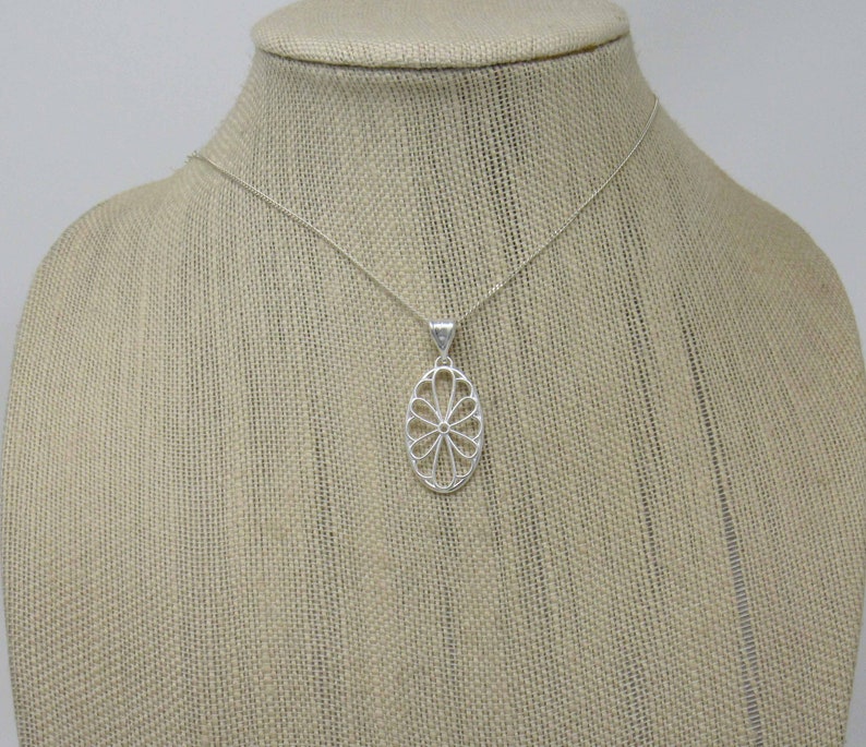 Pu&ograve; includere: Una collana d'argento con un delicato ciondolo ovale con un motivo floreale.