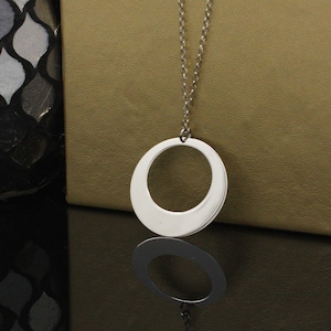 May include: A silver chain necklace with a large, smooth, circular pendant. The pendant has a wide, open circle in the center.