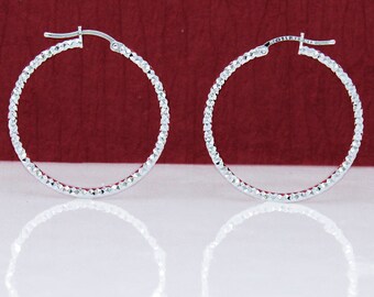 May include: A pair of silver hoop earrings with a textured diamond pattern. The earrings are circular and have a hinged closure.