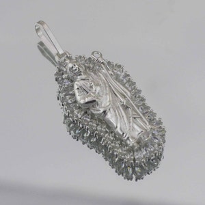 May include: Silver pendant featuring a religious figure surrounded by a halo of clear cubic zirconia stones.