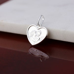 May include: Silver heart-shaped pendant featuring a detailed image of two angels kissing.