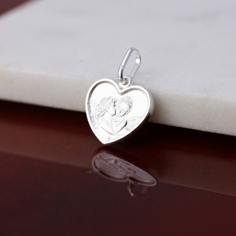 May include: Silver heart-shaped pendant featuring a detailed image of two angels kissing.