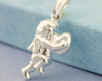 Puede incluir: Un colgante de plata con una figura de ángel detallada con las alas extendidas. El ángel está representado en una pose de vuelo, con una pierna extendida hacia adelante.