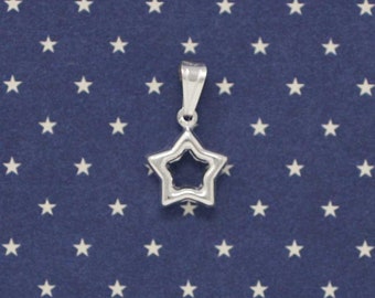 Puede incluir: Un amuleto de plata en forma de estrella de cinco puntas con un centro abierto. El amuleto está sobre un fondo azul con estrellas blancas.
