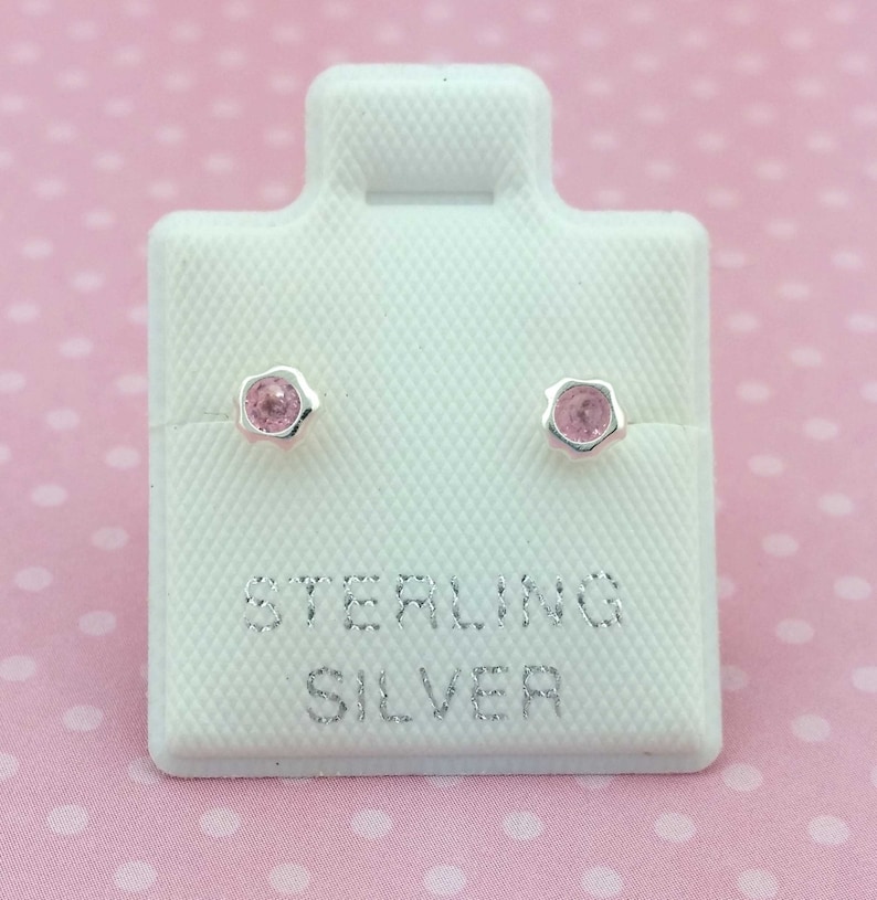 May include: A pair of sterling silver stud earrings with pink stones. The earrings are displayed on a white card with the words "Sterling Silver" printed on it.