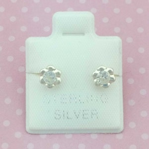 Könnte beinhalten: Ein Paar Ohrstecker aus Sterlingsilber in Blumenform mit klaren Zirkonia-Steinen. Die Ohrringe befinden sich auf einer weißen Karte mit dem Aufdruck "Sterling Silver".