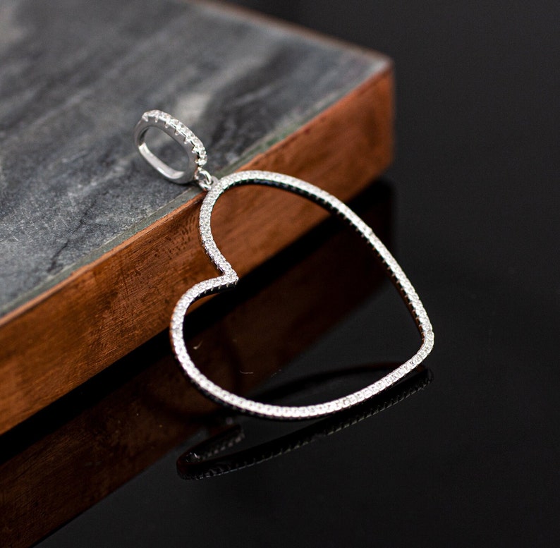Op de afbeelding: Een zilveren hartvormige hanger met een rij kleine, heldere stenen rond de rand.