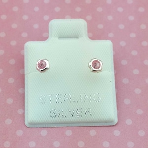 May include: A pair of sterling silver stud earrings with pink gemstones. The earrings are displayed on a white card with the words "Sterling Silver" printed on it.