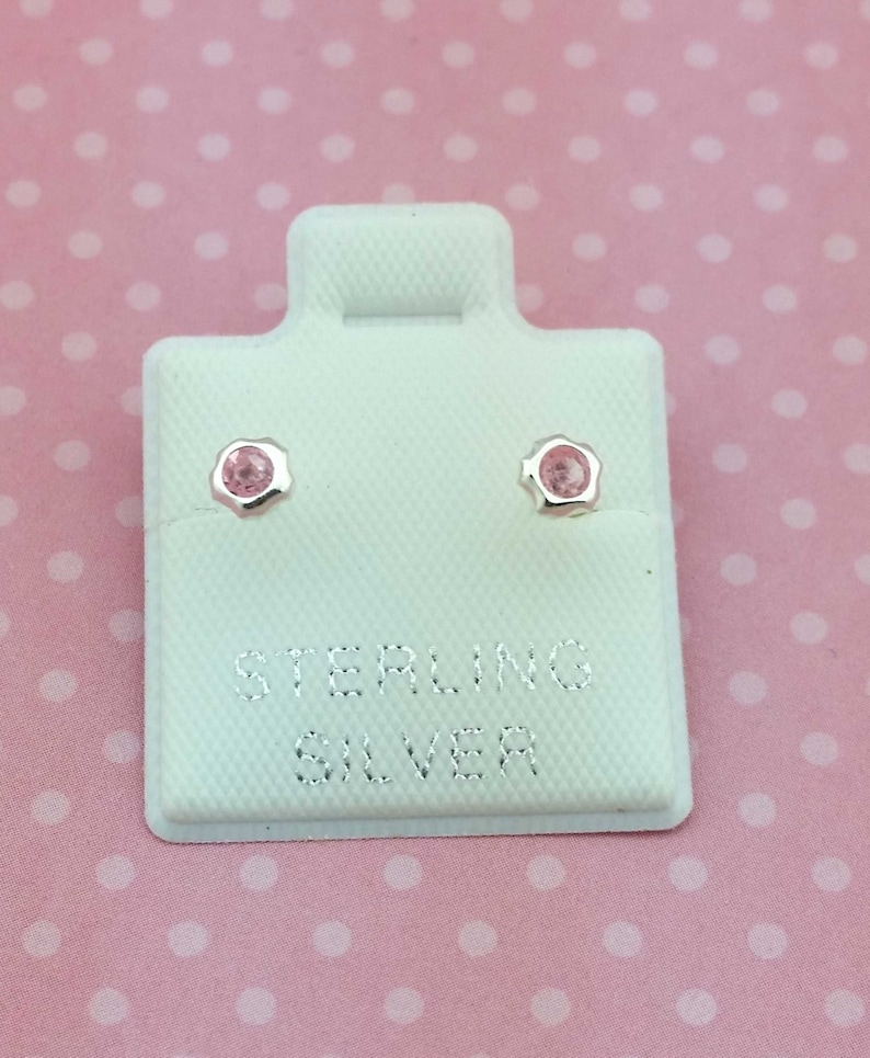 May include: A pair of sterling silver stud earrings with pink gemstones. The earrings are displayed on a white card with the words "Sterling Silver" printed on it.