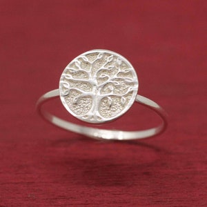 May include: A silver ring with a tree of life design. The ring is oval shaped and the tree is detailed with leaves and branches.