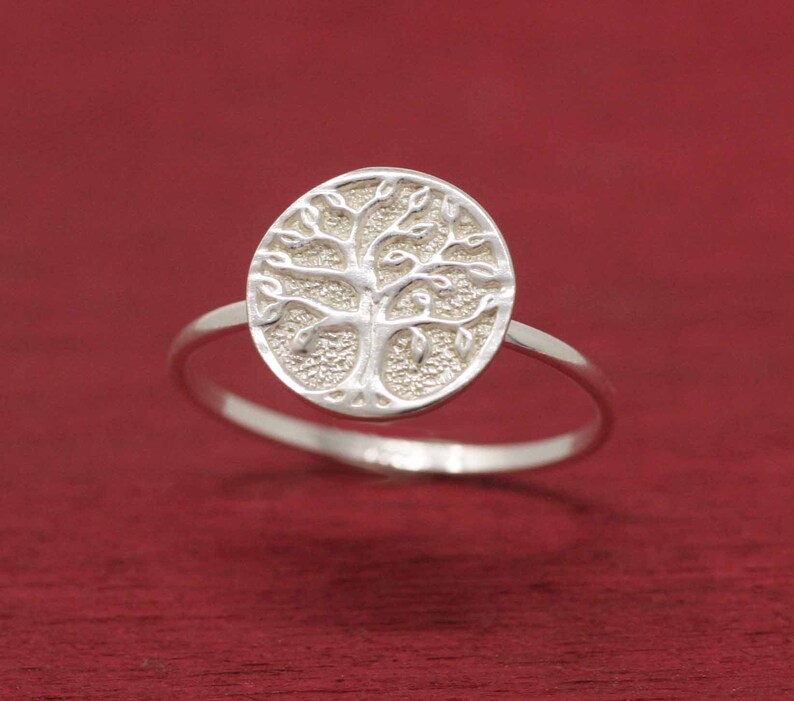May include: A silver ring with a tree of life design. The ring is oval shaped and the tree is detailed with leaves and branches.