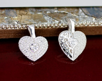May include: Two silver heart-shaped pendants. One pendant is fully encrusted with small, clear stones, with a smaller heart-shaped stone in the center. The other pendant has a half-and-half design, with clear stones on one side and an open filigree design on the other.