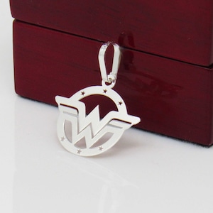May include: Silver pendant featuring the Wonder Woman logo. The logo is a circle with a star design around the edge and a stylized 'W' inside. The pendant has a loop at the top for attaching to a chain.