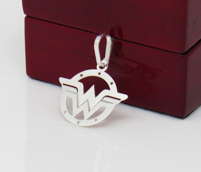 May include: Silver pendant featuring the Wonder Woman logo. The logo is a circle with a star design around the edge and a stylized 'W' inside. The pendant has a loop at the top for attaching to a chain.