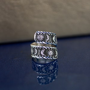 May include: A silver ring with a design of alternating suns and moons. The ring is open and can be adjusted to fit different finger sizes.
