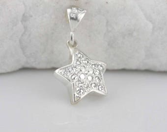 Puede incluir: Un colgante de estrella de plata con una anilla de plata. La estrella está cubierta de pequeños cristales transparentes.