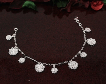 May include: A silver bracelet with a delicate chain and multiple flower-shaped charms. The charms are intricately detailed and have a vintage aesthetic.