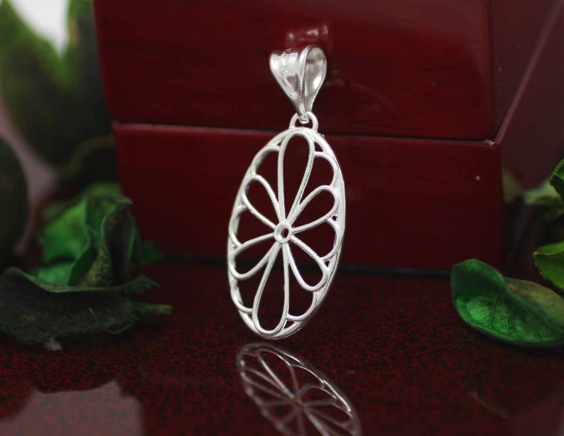 Pu&ograve; includere: Un ciondolo d'argento con un delicato design traforato che ricorda un fiore. Il ciondolo &egrave; di forma ovale e ha un'anellina nella parte superiore per attaccarlo a una catena.