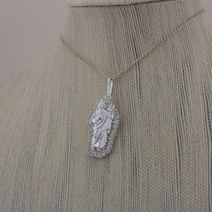 May include: A silver chain necklace with a pendant featuring a detailed image of Jesus Christ. The pendant is surrounded by a decorative border.