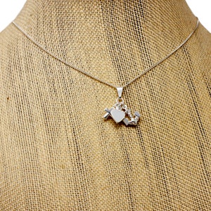 May include: A silver necklace with a heart-shaped pendant and a charm with a cross, a heart, and an anchor.