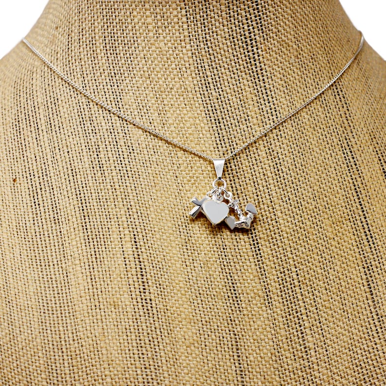 May include: A silver necklace with a heart-shaped pendant and a charm with a cross, a heart, and an anchor.