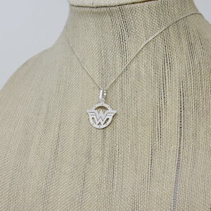 May include: A silver necklace with a Wonder Woman logo pendant. The pendant is a circular cutout of the logo with a detailed design.