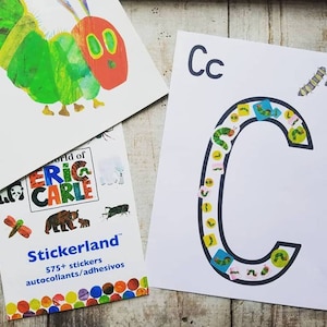 May include: A white sheet of paper with the letter C printed in black. The letter is filled with colorful stickers of caterpillars. The text "Cc" is printed at the top of the page.