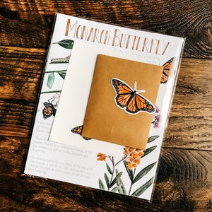 May include: A white card with the text "Monarch Butterfly" and a description of the butterfly. The card features a brown envelope with a sticker of an orange and black monarch butterfly.