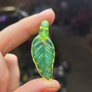 May include: A bright green glass leaf charm pendant. The leaf has a detailed vein pattern and a shiny finish.