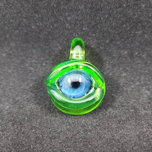 May include: A green glass pendant with a blue eye design. The pendant has a loop at the top for hanging.