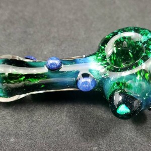 May include: A green glass smoking pipe with blue glass accents. The pipe has a swirl design and a round bowl.