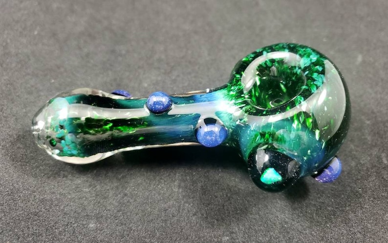 May include: A green glass smoking pipe with blue glass accents. The pipe has a swirl design and a round bowl.