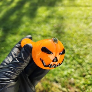 May include: Orange glass pipe shaped like a pumpkin with a black and white jack-o'-lantern face.