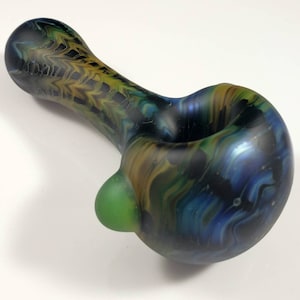 May include: A glass pipe with a black, blue, green, and gold swirl pattern. The bowl of the pipe is round and has a green accent.