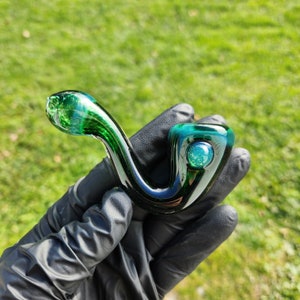 Op de afbeelding: Een groene glazen pijp met een ronde, iriserende kom. De pijp heeft een donkergroen swirl-patroon en een heldere glassteel.