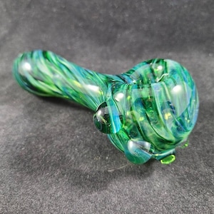 May include: A hand-blown glass pipe with a swirling pattern of green and blue hues. The pipe features a bowl, a stem, and a mouthpiece, all crafted from transparent glass. The design includes small, rounded glass accents.