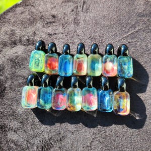 May include: A collection of small, colorful glass bottles with black stoppers. The bottles are filled with swirling shades of blue, red, yellow, and green. The bottles are arranged in rows on a dark, textured surface.