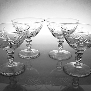 May include: A set of four clear glass coupes featuring a delicate etched leaf and vine pattern on the bowls. Each glass has a distinctive twisted stem design and a circular base, providing a consistent look across the entire collection of glassware.