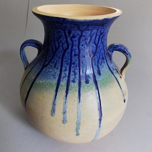 May include: A ceramic vase with two handles, featuring a wide, flared rim and a rounded body. The upper portion is glazed in a deep blue with vertical drip patterns that transition into a band of green, fading into a light beige base color.